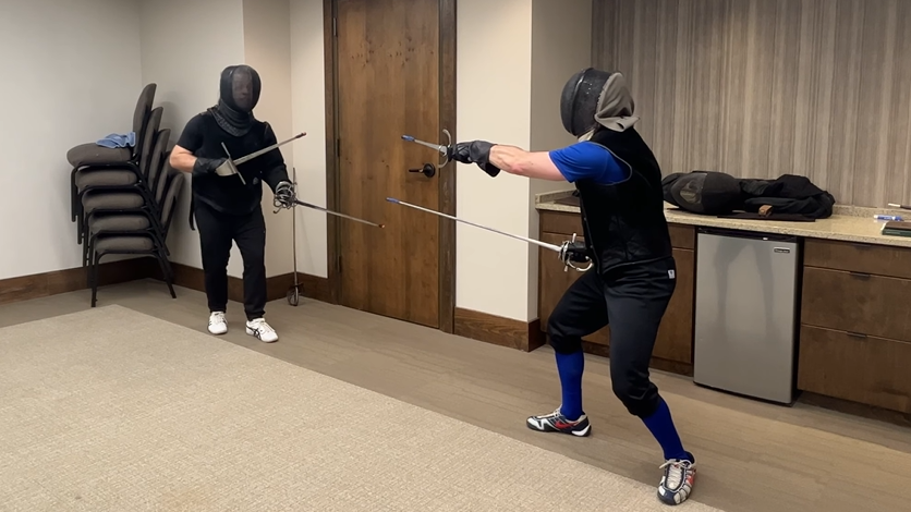 Justin in a Marcelli rapier & dagger stance, sword very withdrawn and dagger extended, taking a lesson with Maestro David Coblentz at RASP 2023.